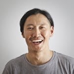 A joyful Asian man laughing against a neutral gray backdrop.